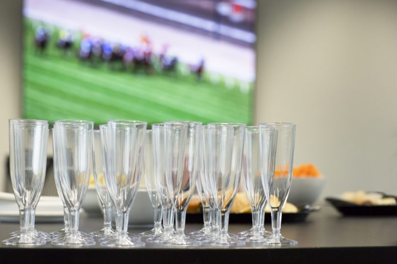 Champagne glasses on a table with horse race on television in background.