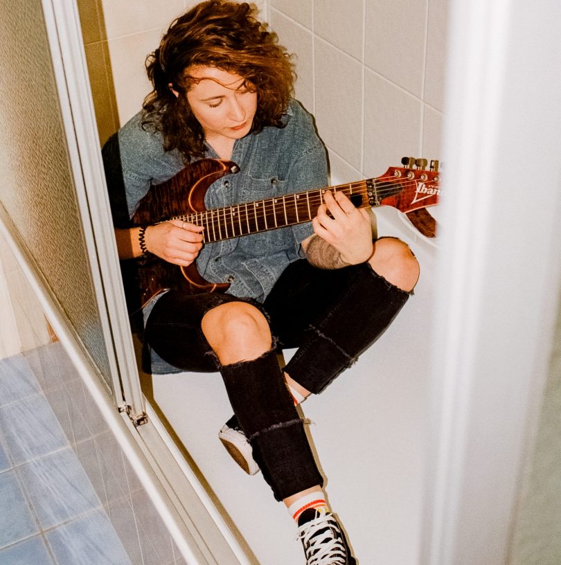 Photograph shows Hope Wilkins sitting in the bath with her guitar