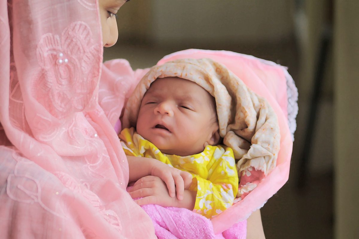 Woman holding baby, with pink shawl wrapped around her head and her baby