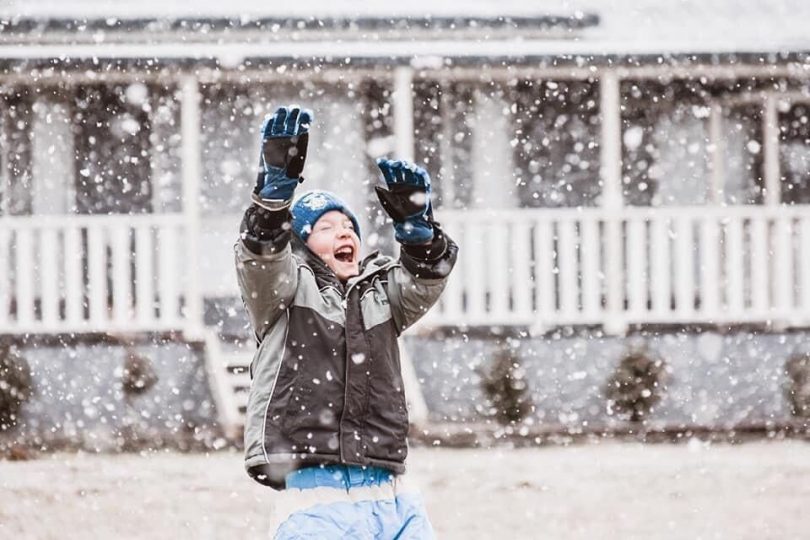 A boy smiles as he plays in falling snow