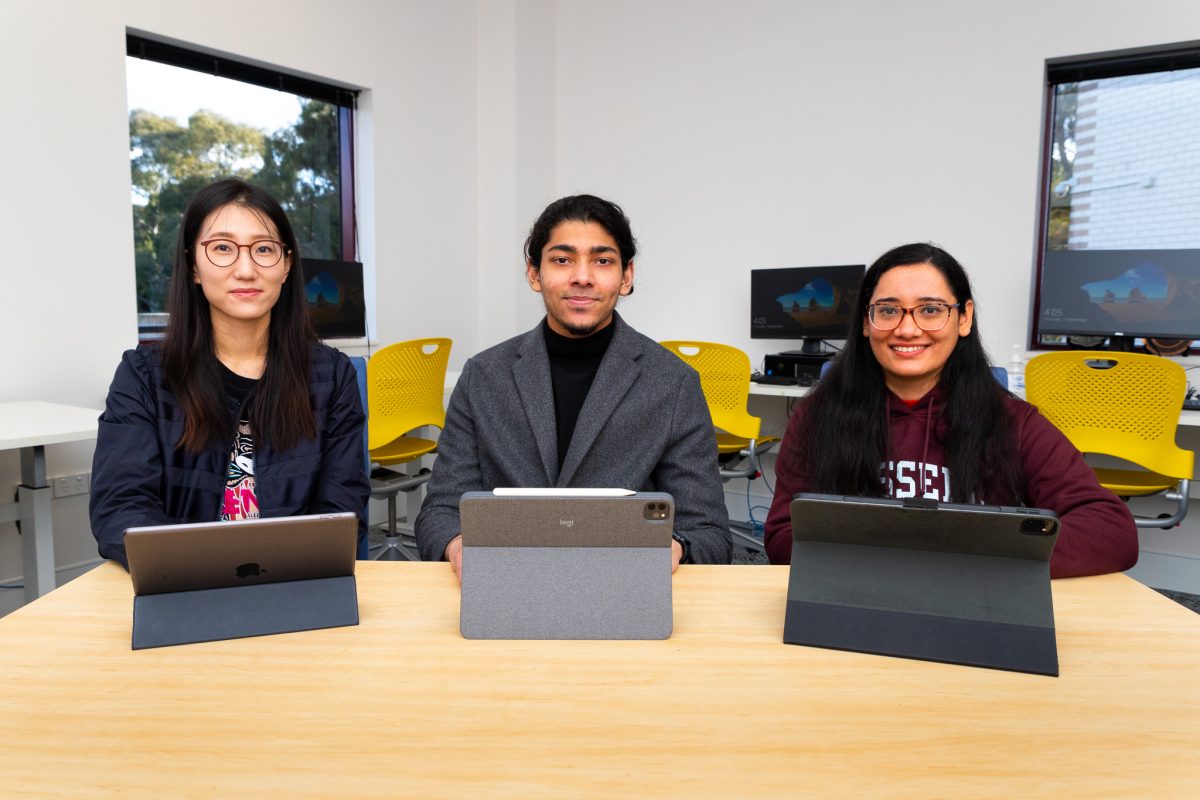 Three students sitting in front of their tablets and smiling at the camera