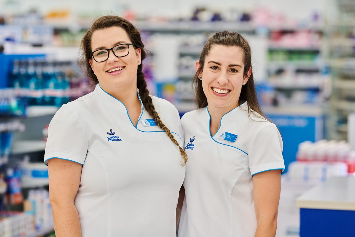 Two pharmacists in uniform, smiling in a pharmacy