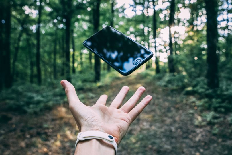 Hand throwing mobile phone in forest.